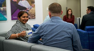 woman smiling at a male sat down in a waiting room holding an Elanco mug