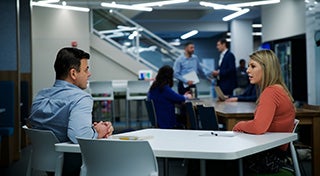 two people talking at a table in an office setting
