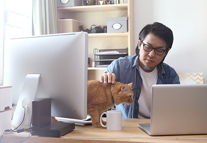 a man sat at a desk whilst stroking his cat on the desk