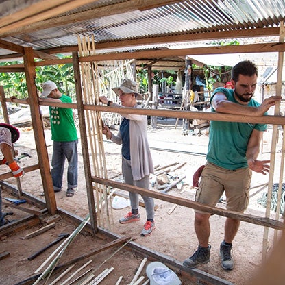two men and a woman fixing bamboo sticks to a wall frame