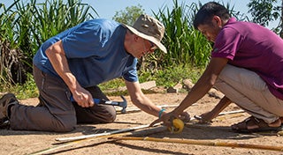 Deux hommes s'agenouillent pour fabriquer un objet en bambou.