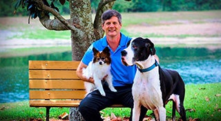 a man sat on a bench holding a small dog whilst petting a large dog