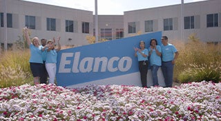 a group of five stood next to an Elanco animal health sign outside in front of flowers