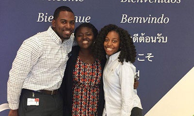 two women and a male smiling in front of a welcome sign