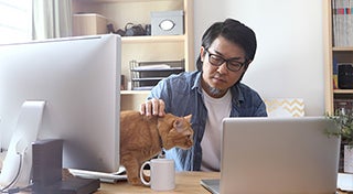 a man sat at a desk whilst stroking his cat on the desk