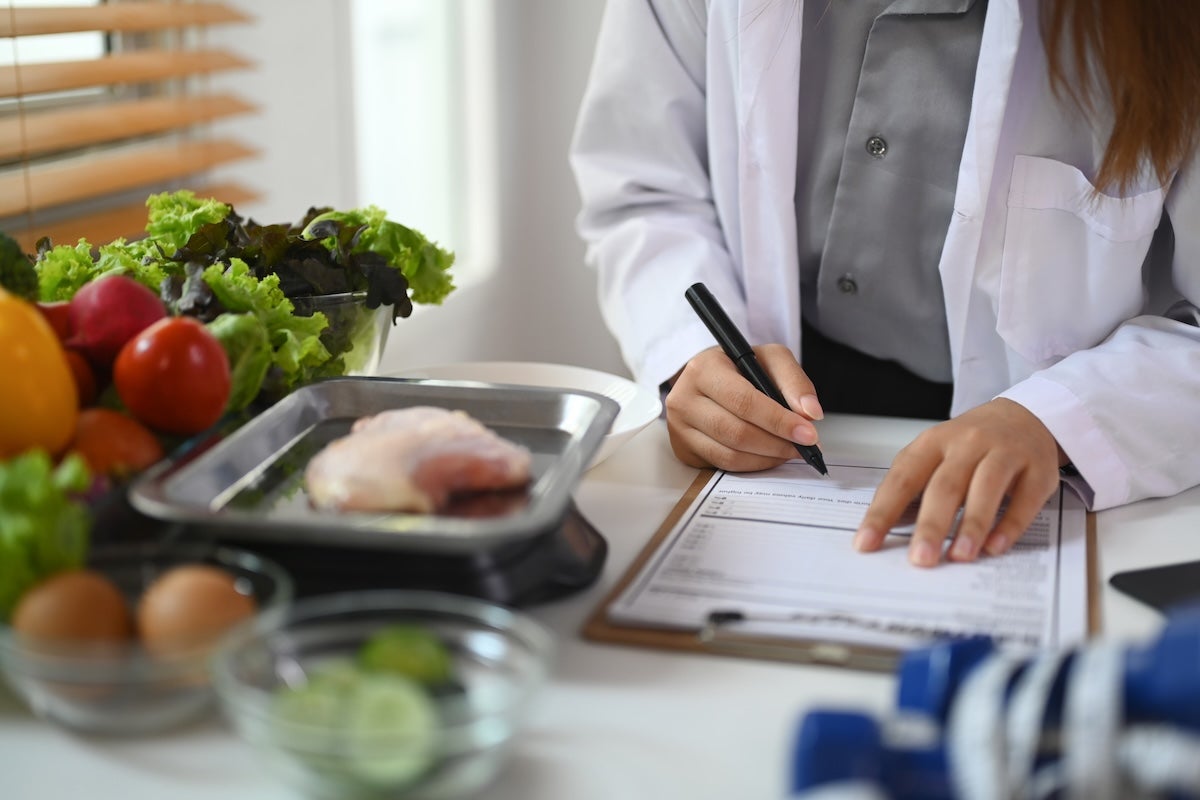 A scientist writes on a clipboard with various foods in bowls and dishes on the counter in front of her