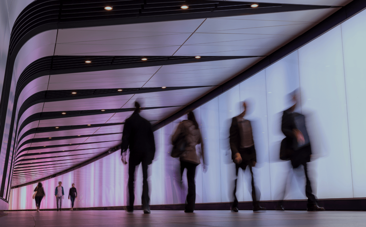 People walking in a hallway in an office building with floor to ceiling windows