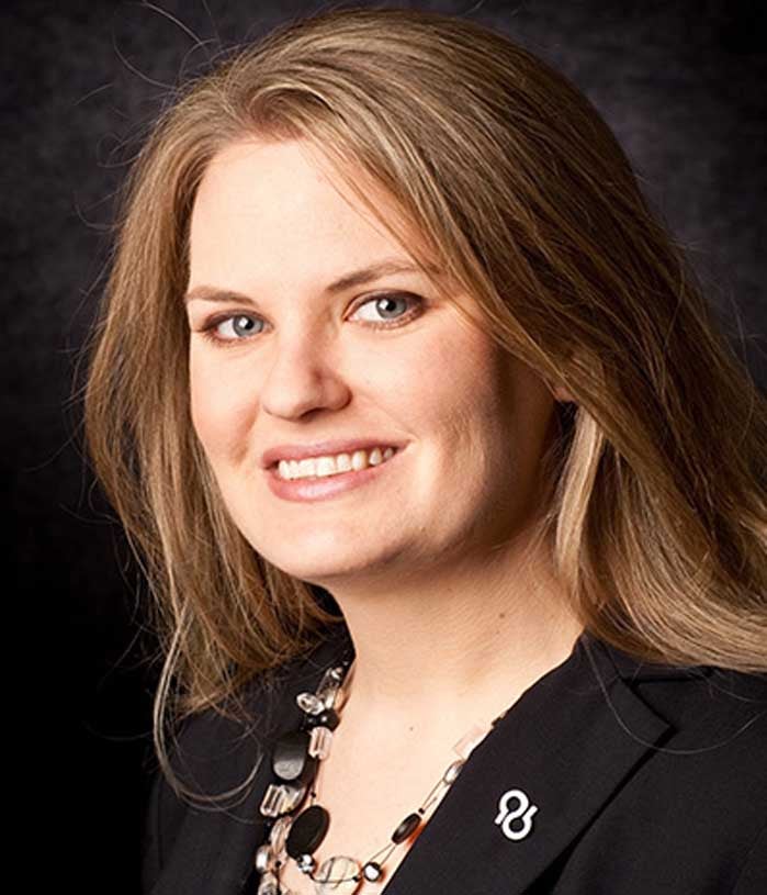 Heather Snyder, a woman with dark blonde hair, wears a black blazer on a black background.