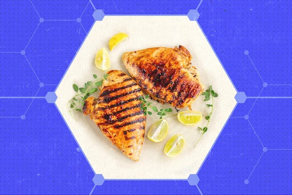 Grilled chicken, herbs, and lemon slices on a white hexagonal plate in front of a blue background