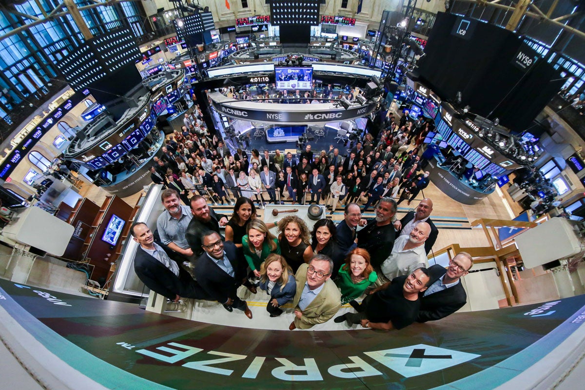 A fisheye view from above of XPRIZE CEO Anousheh, plus XPRIZE employees and supporters, from the balcony of the NYSE closing bell. The entirety of the Stock Exchange trading floor is visible.