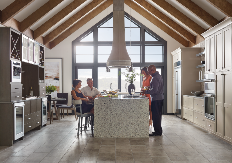 A group of friends around a kitchen island with a window in the back.