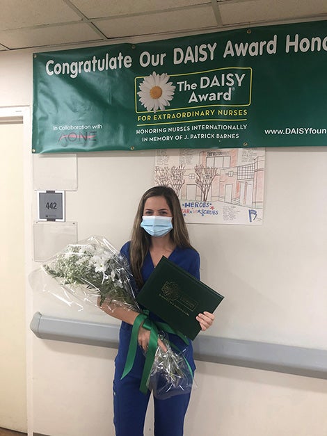 Brittney Ellis in scrubs and mask holding bouquet of flowers and award