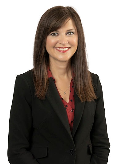 Dana Harrison with long dark hair wearing a dark business suit and red blouse.