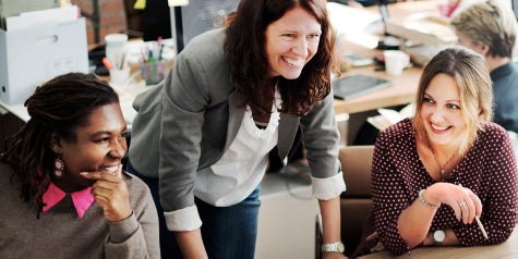 Three diverse women smiling and communicating in a work meeting.