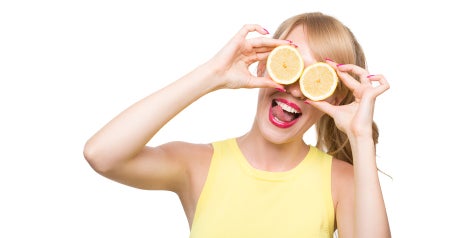 Young lady holding oranges cut in half in front of here eyes smiling.