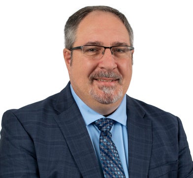 Head and shoulders photo of Paul brown with goatee wearing gray suit, blue shirt and tie, glasses
