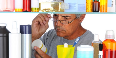 Man searching through medicine cabinet and examining label of medicine