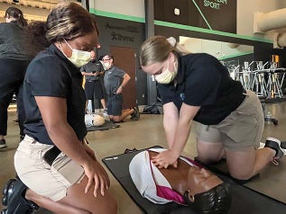 Two athletic trainers giving a fake person chest compressions.