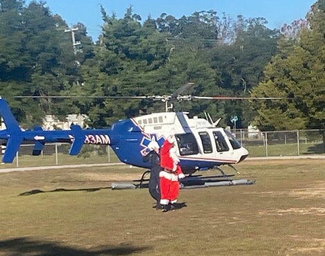 This picture shows Santa Claus waving in front of a helicopter that just landed in an open field.