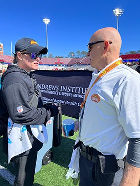 Two athletic trainers are talking at an outdoor stadium.