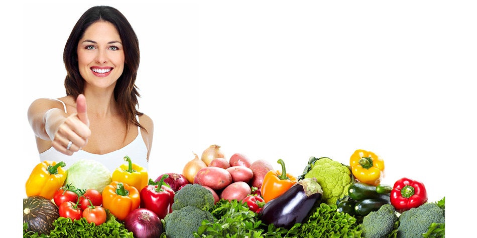 Woman holding her thumb up in front a mixed, colorful area of vegetables like bell peppers, broccoli and more