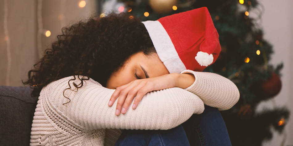 Woman wearing Santa hat with her head down overwhelmed with tree in background