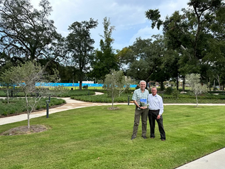 Doctor and project manager pose proudly in front of olive trees planted on new hospital campus to symbolize culture.