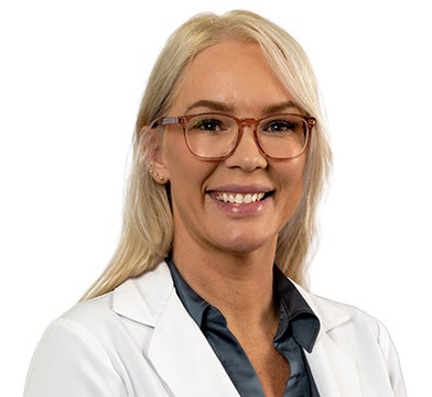 Dr. Flores is pictured smiling in her physician's coat. She has blonde hair and glasses.