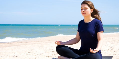 Woman sitting on beach with legs crossed meditating and practicing yoga