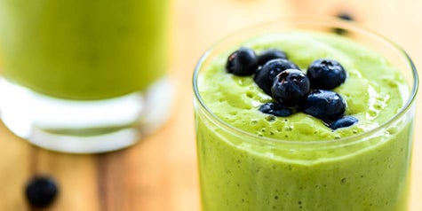 Green drink filled with fruits and veggies, topped with blueberries 