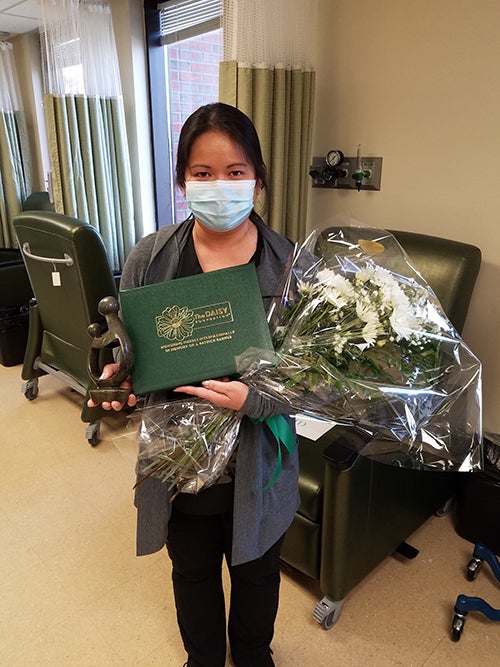Alma Flores in scrubs holding DAISY award and flower bouquet