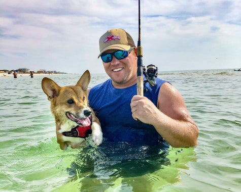 ECMO patient Austin Luke standing in the Gulf holding a corgi dog and fishing pole.