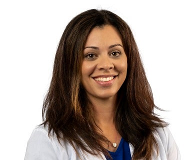 Shirley Blanco is pictured in her white coat, smiling. She has dark hair that comes past her shoulders. 