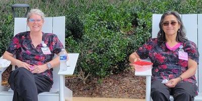 Mammography technicians Suzanne and Margarita sit outside in picnic chairs.