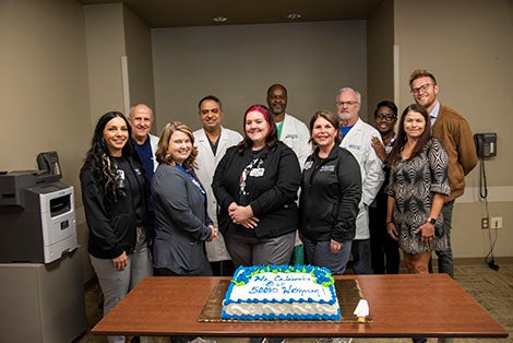 Physicians and staff posing in front of cake
