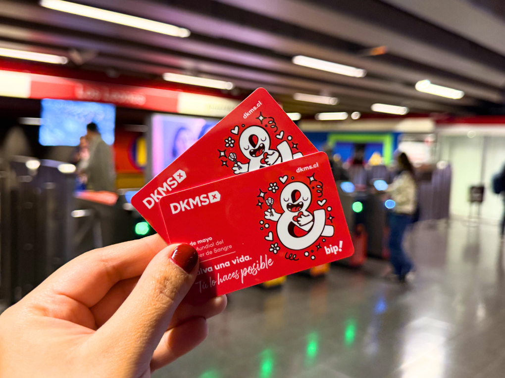 Mano sosteniendo dos tarjetas Bip conmemorativas de DKMS en una estación de Metro de Santiago Mano sosteniendo dos tarjetas Bip conmemorativas de DKMS en una estación de Metro de Santiago