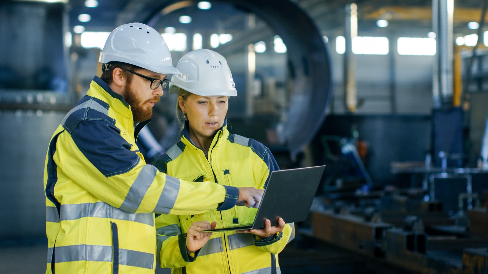 Two colleagues in hard hats and high viz jackets in a factory setting