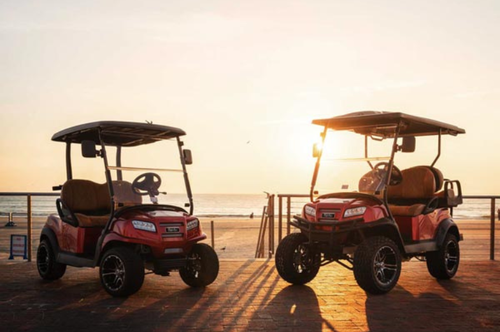 Two red Club Car special edition golf carts parked outside at sunset
