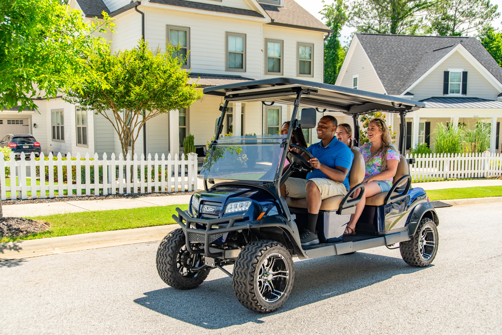 Four people drive in a Club Car Onward down a neighborhood street.
