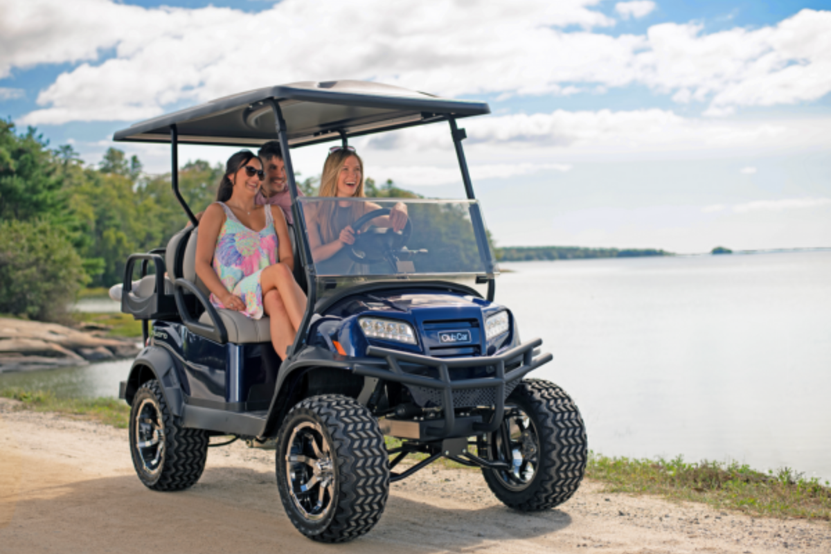 A group drives a lifted Club Car Onward 4 passenger on a path along a lake.