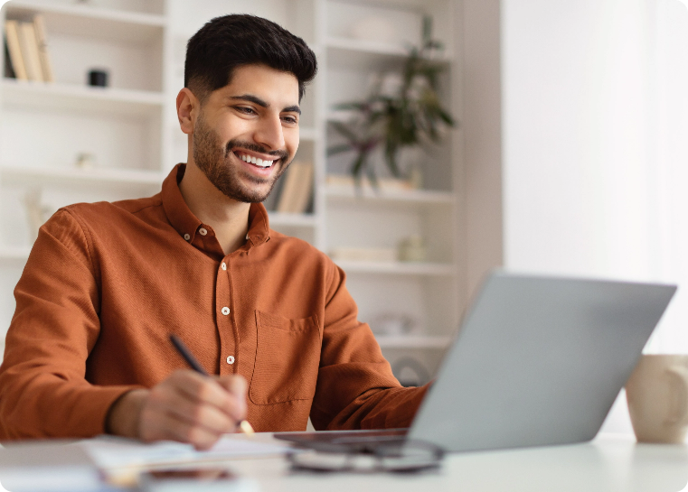 Man looking at a laptop smiling and taking notes
