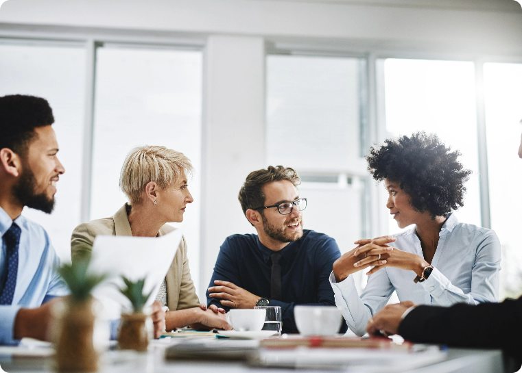 Group of people sitting at a table with coffee mugs and papers while have a conversation