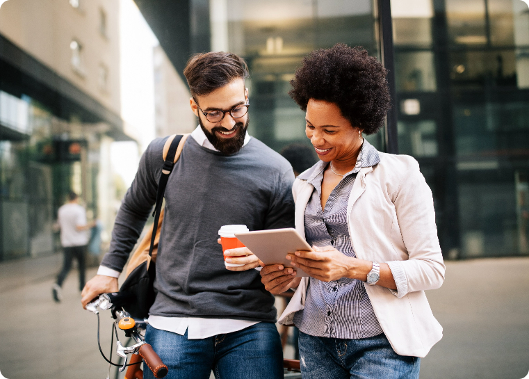 A man holding a leaning bike and a woman standing next to him looking at a tablet and smiling