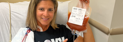 DKMS donor Alyson sitting in the hospital chair smiling and holding her blood stem cell donation bag.