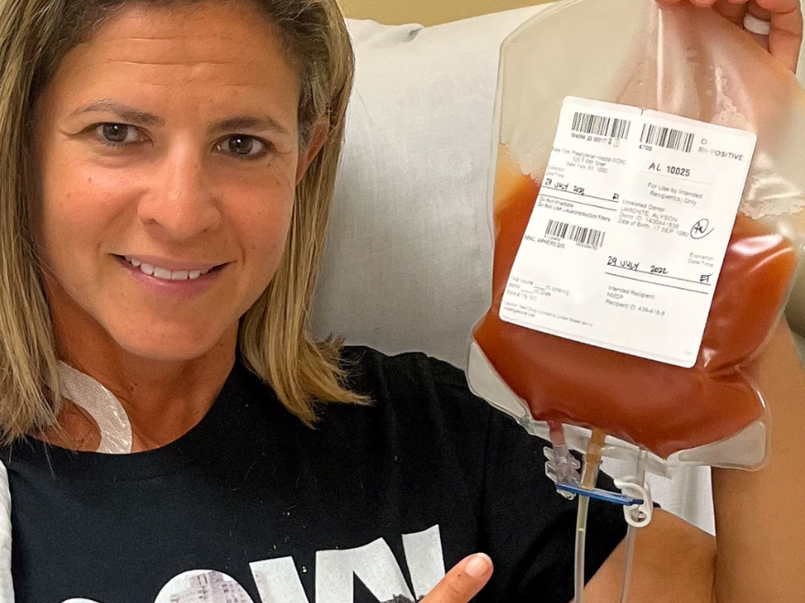 DKMS donor Alyson sitting in the hospital chair smiling and holding her blood stem cell donation bag. DKMS donor Alyson sitting in the hospital chair smiling and holding her blood stem cell donation bag.