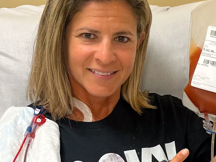 DKMS donor Alyson sitting in the hospital chair smiling and holding her blood stem cell donation bag. DKMS donor Alyson sitting in the hospital chair smiling and holding her blood stem cell donation bag.