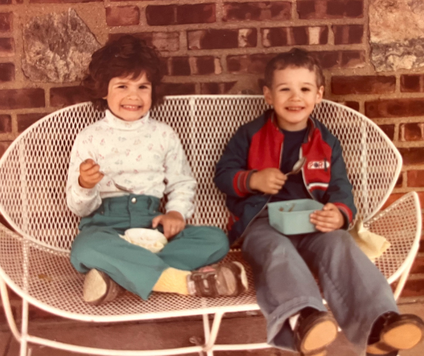Alyson as a young child sitting on a white bench with Micheal on her right as a young child