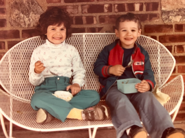 Alyson as a young child sitting on a white bench with Micheal on her right as a young child