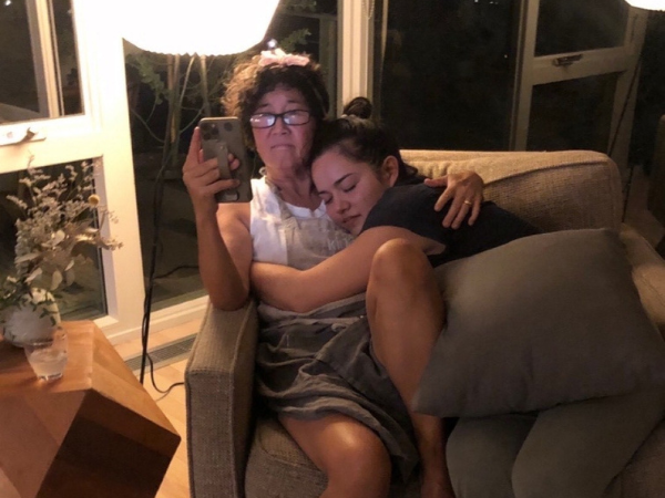 Mama G and Emi Grannis are both sitting in a chair at night with the light on. Emi is curled up in Mama G's lap on her right side. 