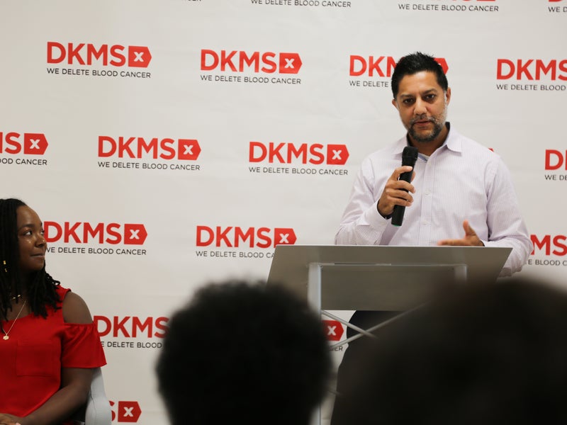 Dr. Nilay Shah, Transplant Physician, standing at a podium speaking in front of a dkms banner